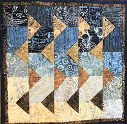 An image of a quilt with gold triangle patterns and navy blue squares.